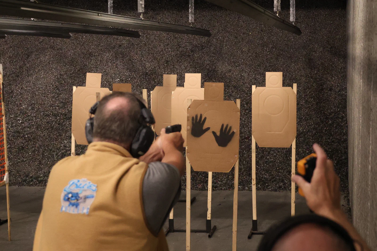 A shooter firing at targets while a Safety Officer holds a timer behind them