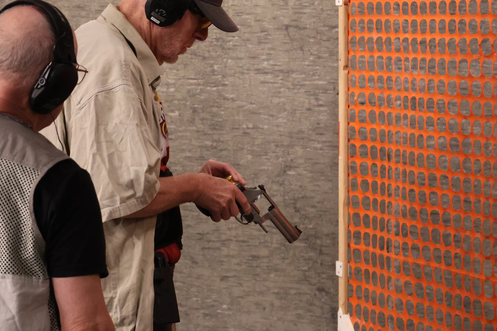 A shooter loading a revolver while a Safety Officer looks on