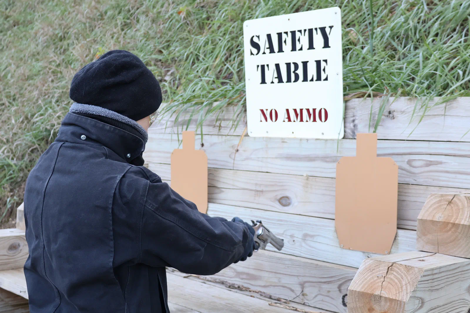 A shooter in a dark jacket and hat checking a revolver at the Safety Table