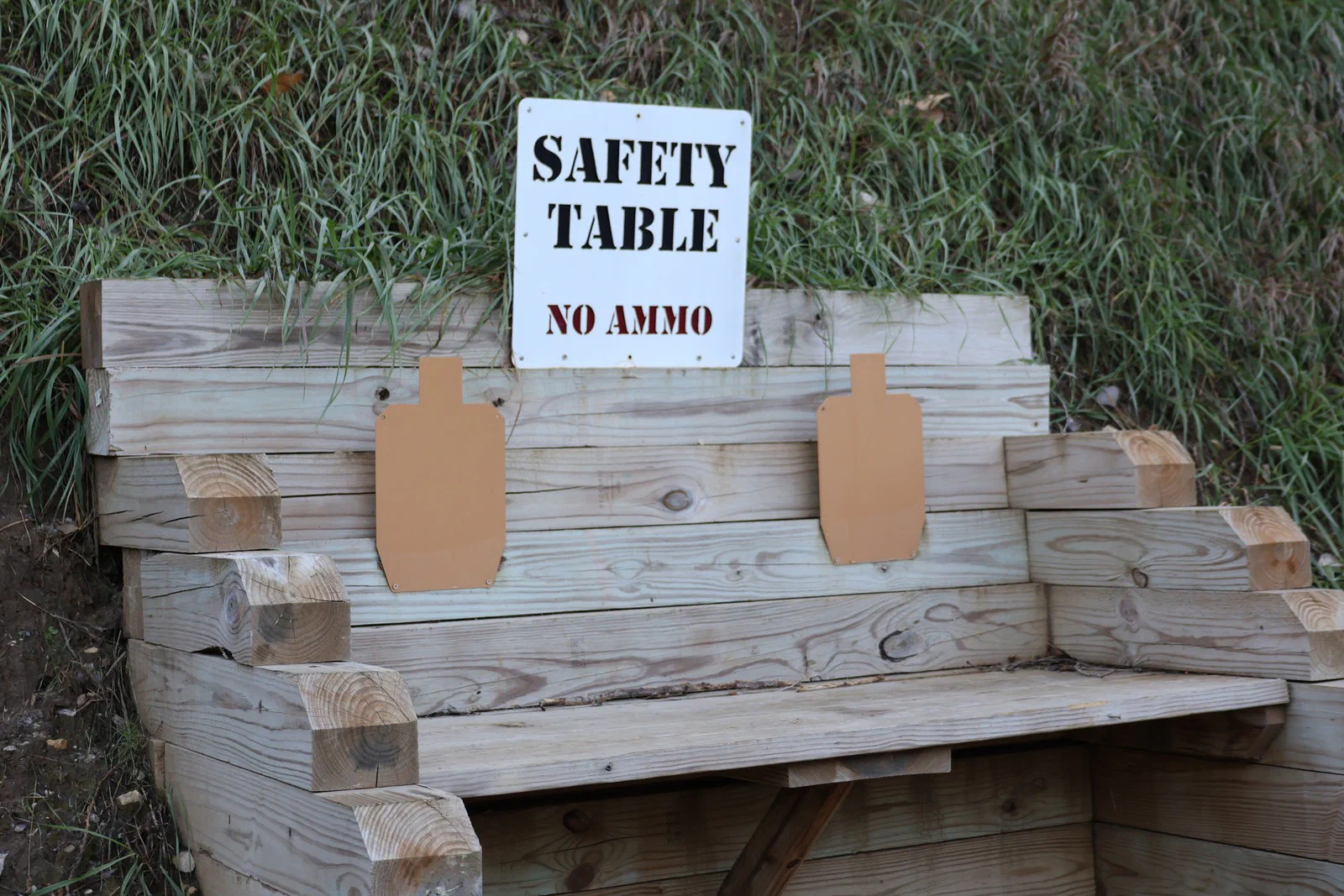A white sign reading Safety Table, No Ammo above a wooden bench