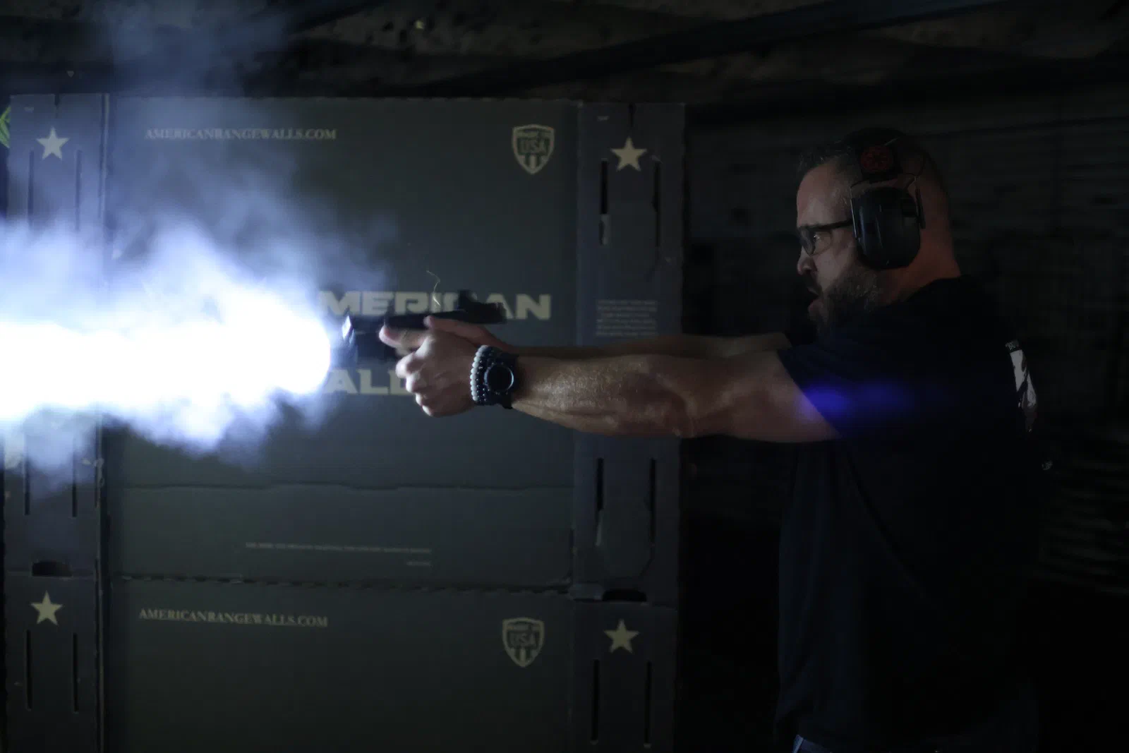 A shooter firing in a dark bay, with the beam of a weapon-mounted light cutting through the smoke